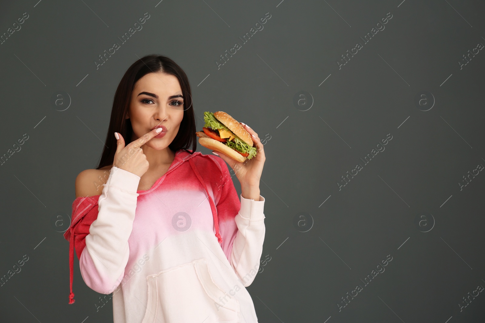 Photo of Young woman eating tasty burger on grey background. Space for text
