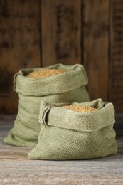 Photo of Burlap bags with uncooked bulgur on wooden table