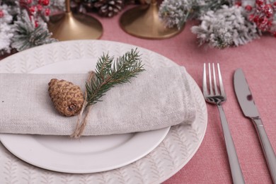 Festive place setting with beautiful dishware, cutlery and cone for Christmas dinner on pink tablecloth, closeup