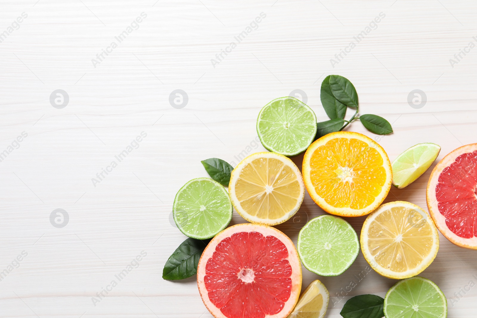 Photo of Different cut citrus fruits and leaves on white wooden table, flat lay. Space for text