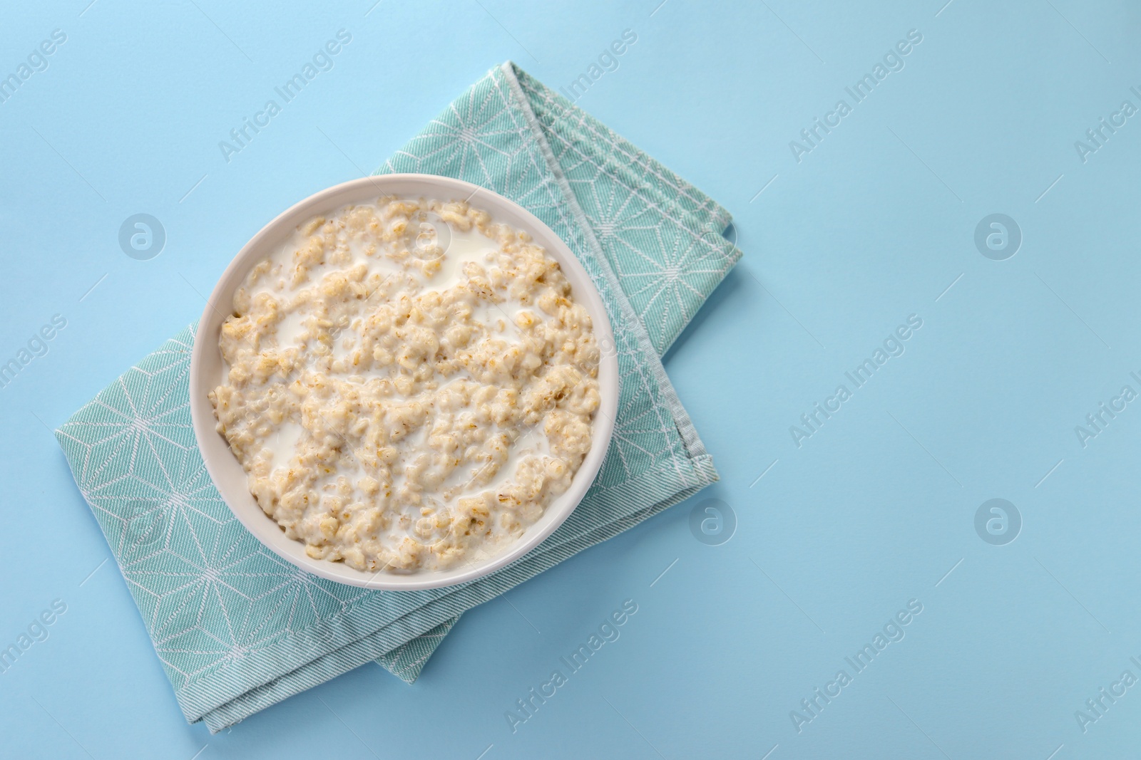 Photo of Tasty boiled oatmeal in bowl on light blue table, top view. Space for text