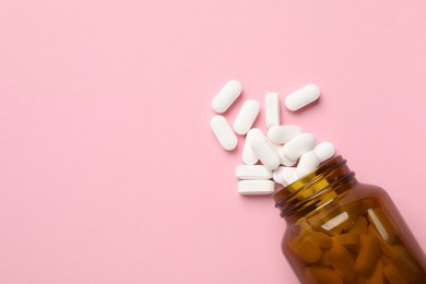 Photo of Bottle and vitamin capsules on pink background, top view. Space for text