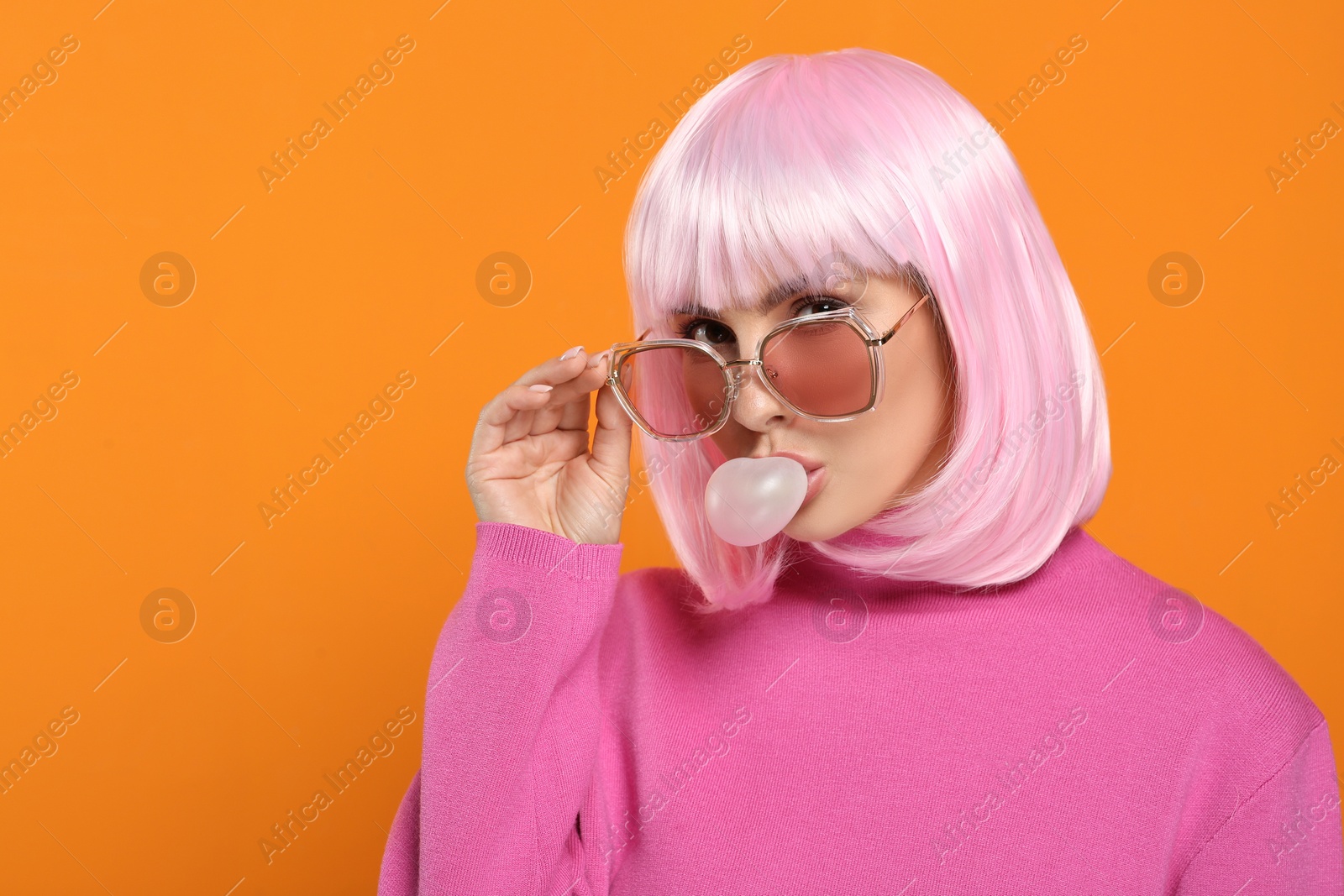 Photo of Beautiful woman in sunglasses blowing bubble gum on orange background, space for text