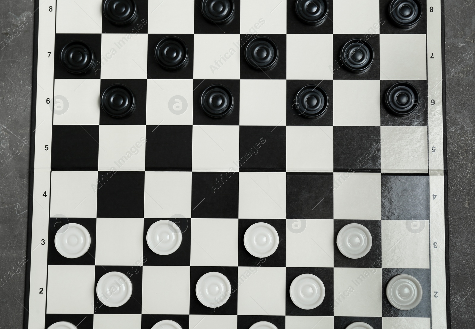 Photo of Checkerboard with game pieces on grey table, top view