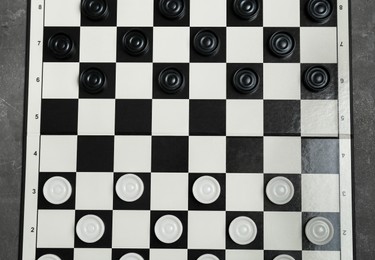 Photo of Checkerboard with game pieces on grey table, top view