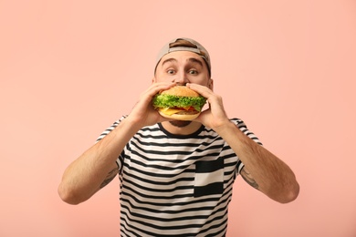 Young man eating tasty burger on color background