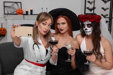 Group of women in scary costumes with cocktails taking selfie at Halloween party indoors