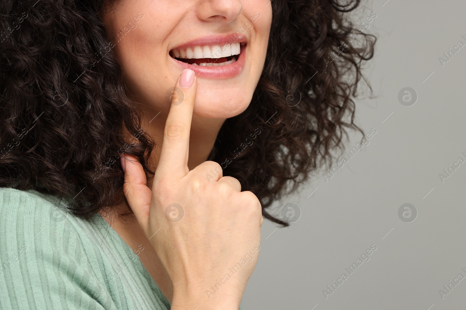 Photo of Young woman showing her teeth with whitening strip on grey background, closeup. Space for text