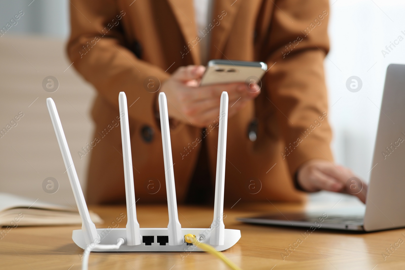 Photo of Woman with smartphone and laptop connecting to internet via Wi-Fi router at table indoors, selective focus