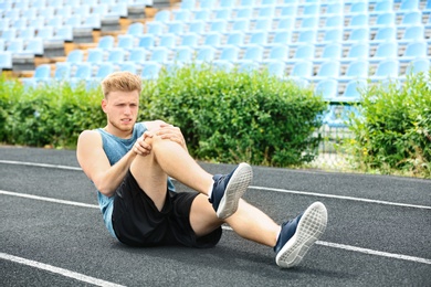 Photo of Man in sportswear suffering from knee pain at stadium