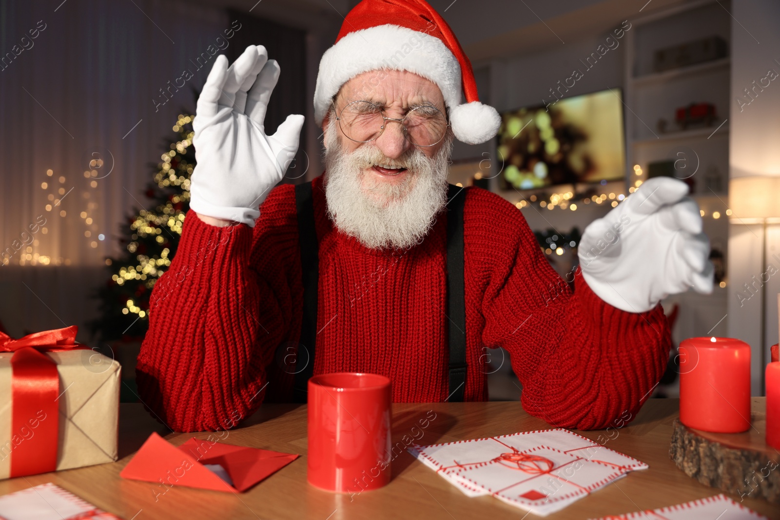 Photo of Laughing Santa Claus at his workplace. Letters and cup of hot beverage on table in room decorated for Christmas
