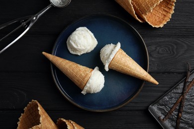Photo of Ice cream scoops in wafer cones on black wooden table, flat lay