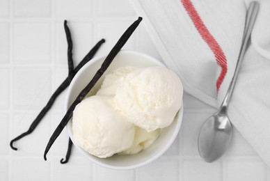 Photo of Delicious ice cream, spoon and vanilla pods on white tiled table, flat lay