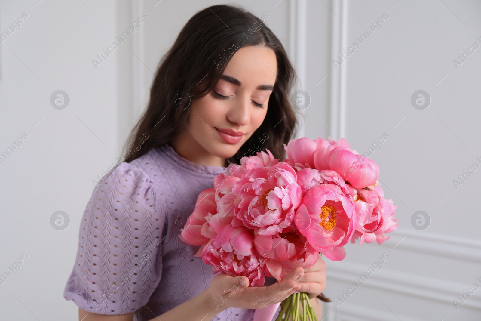 Photo of Beautiful young woman with bouquet of pink peonies near white wall