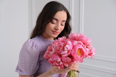 Beautiful young woman with bouquet of pink peonies near white wall