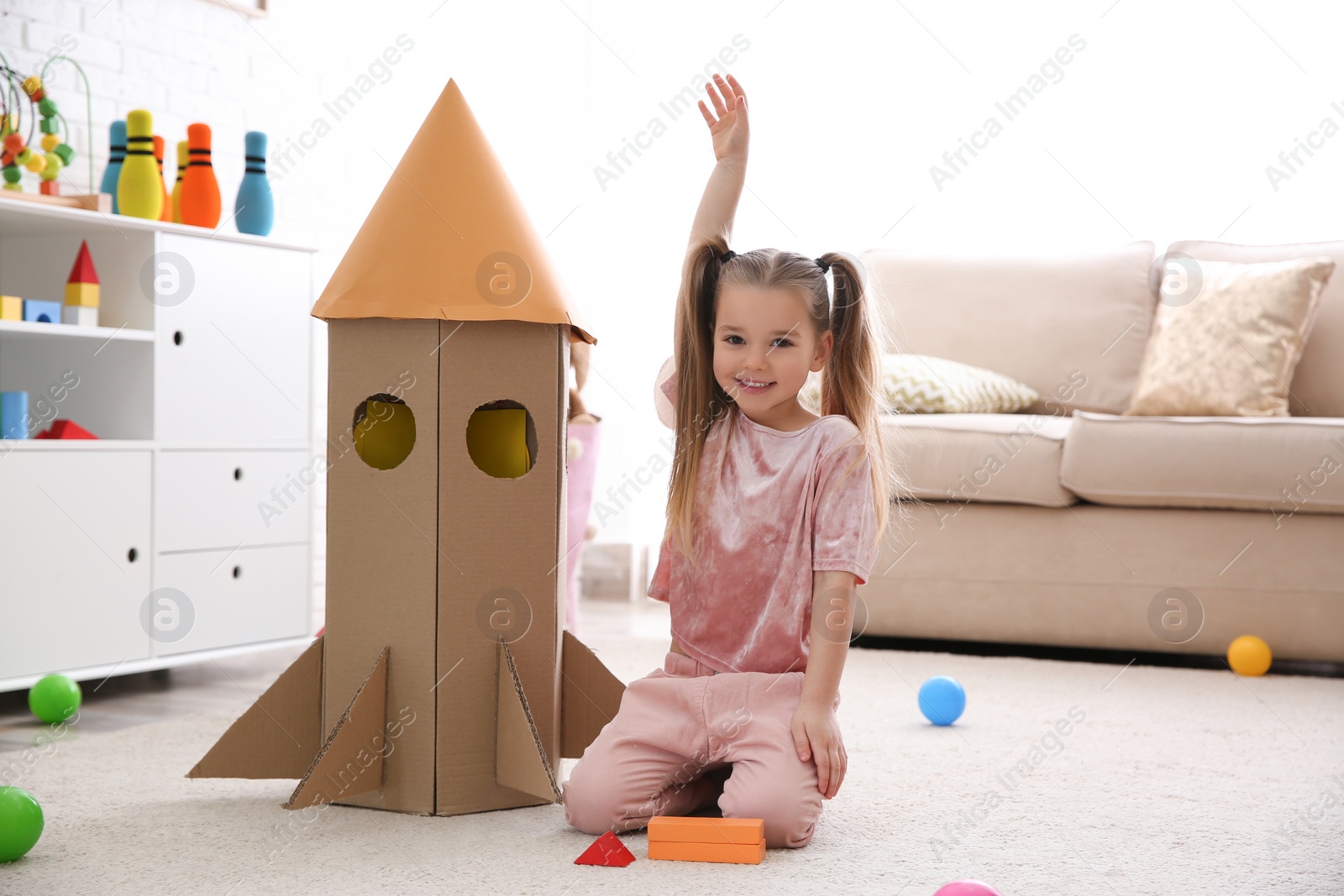 Photo of Cute little child playing with cardboard rocket at home