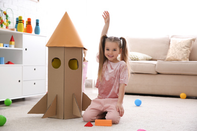 Cute little child playing with cardboard rocket at home