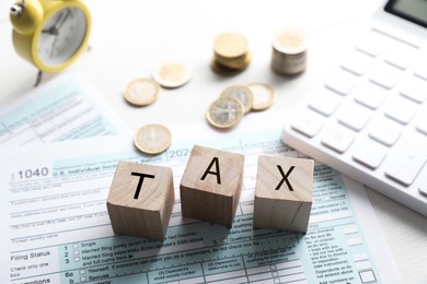 Photo of Wooden cubes with word Tax, documents, calculator and coins on white table, closeup