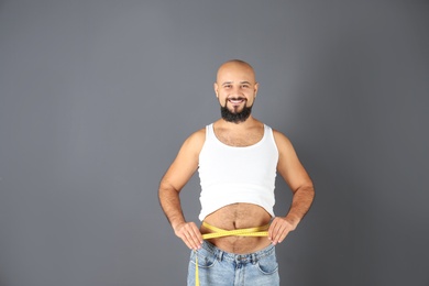 Overweight man with measuring tape on gray background