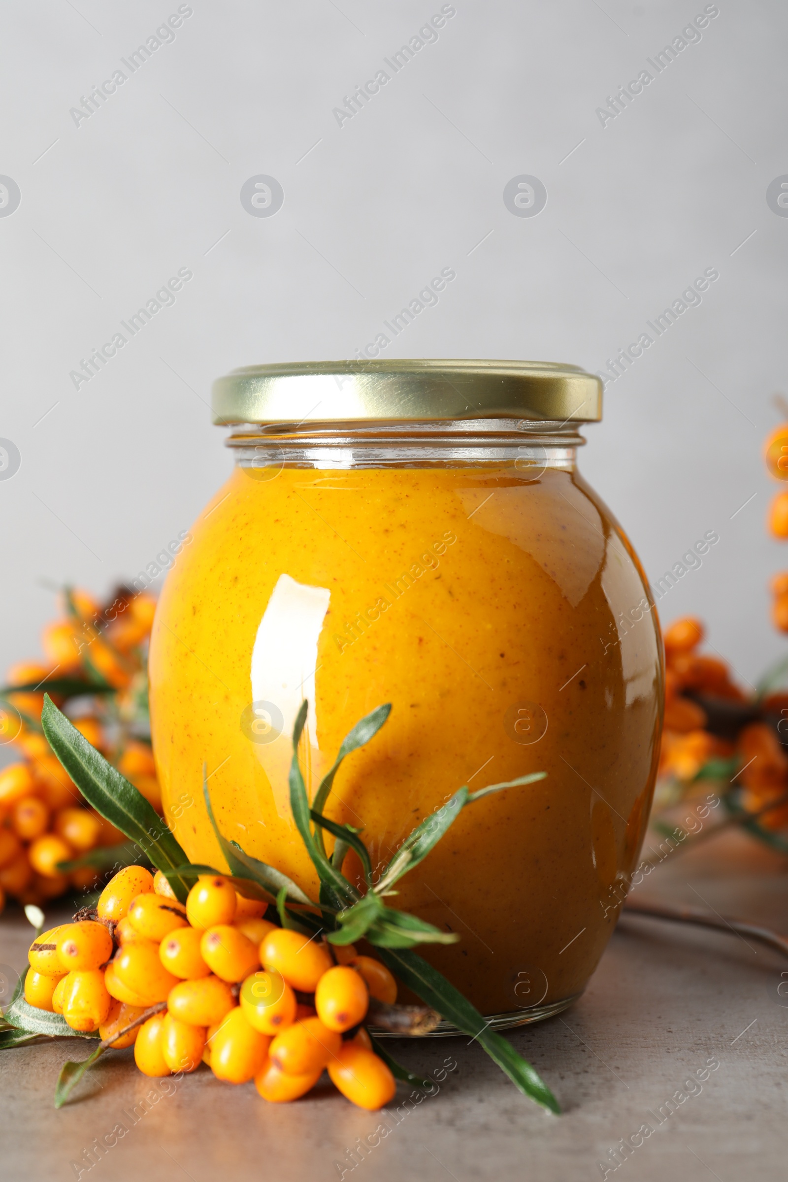 Photo of Delicious sea buckthorn jam and fresh berries on grey table