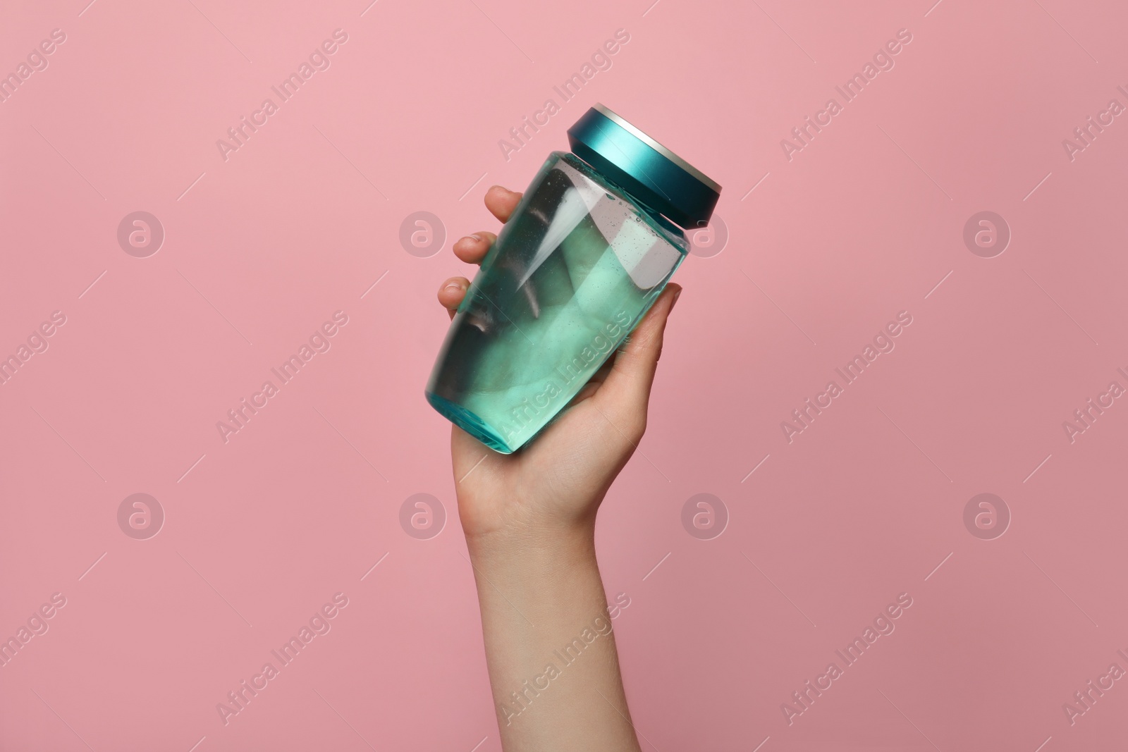 Photo of Woman holding bottle of hair care cosmetic product on pink background, closeup