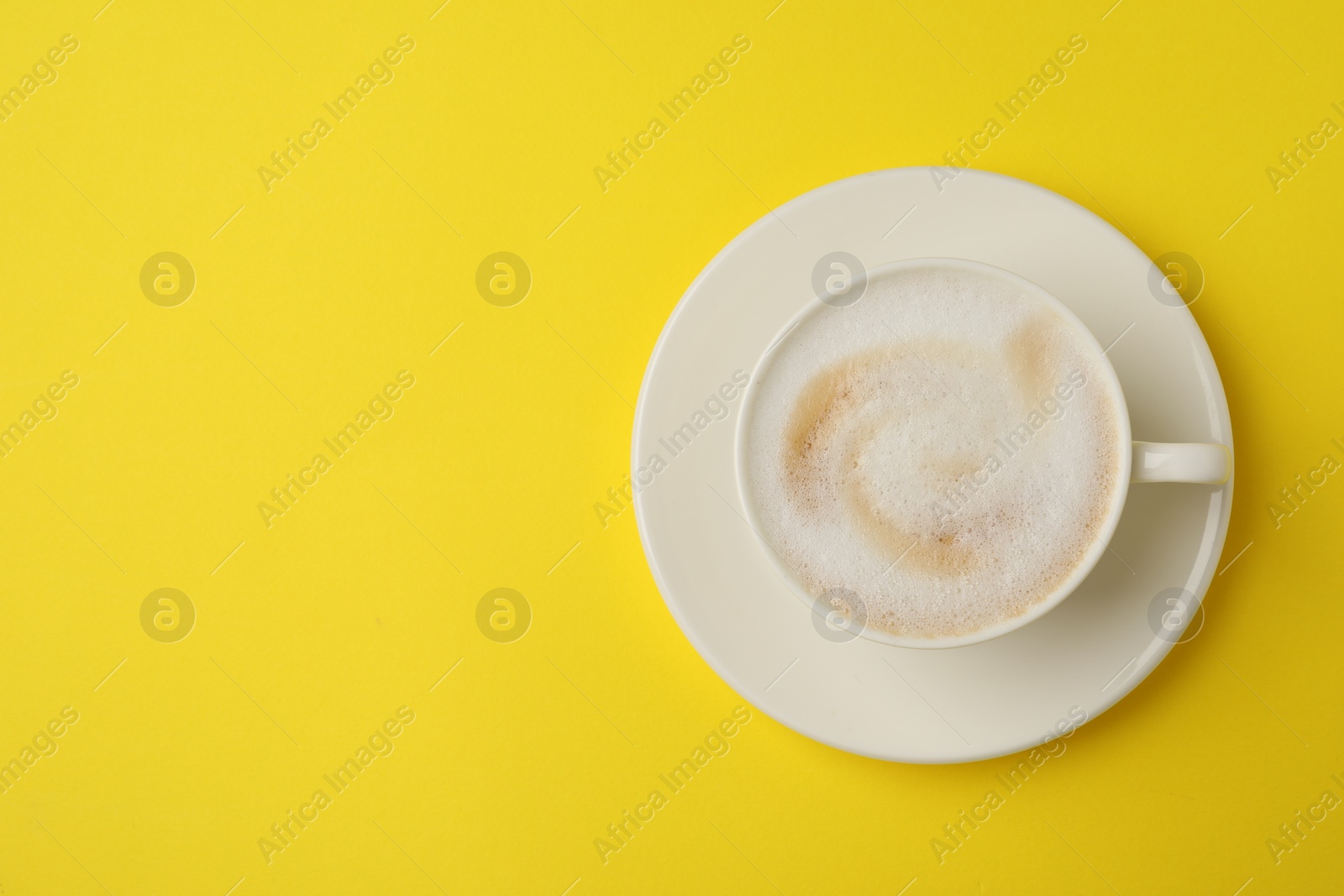 Photo of Tasty cappuccino in coffee cup on yellow background, top view. Space for text