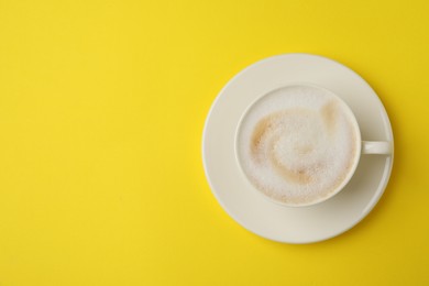 Photo of Tasty cappuccino in coffee cup on yellow background, top view. Space for text