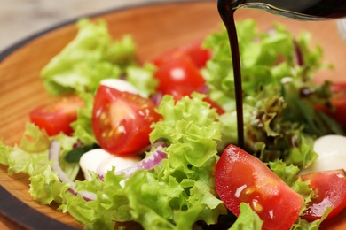 Photo of Pouring balsamic vinegar onto fresh vegetable salad on plate, closeup