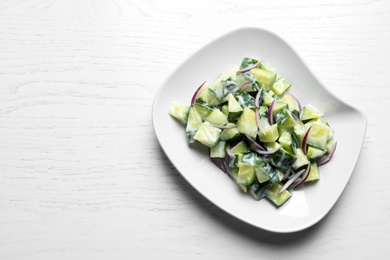 Photo of Plate with fresh creamy cucumber salad on white wooden background, top view. Space for text