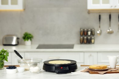 Photo of Electric maker with crepe and ingredients on white marble table in kitchen