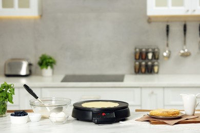 Electric maker with crepe and ingredients on white marble table in kitchen