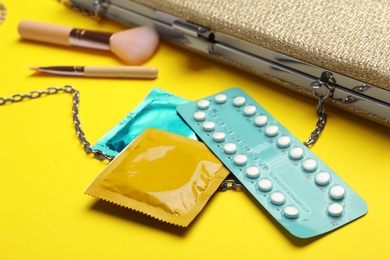 Condoms and birth control pills on yellow background, closeup. Safe sex concept