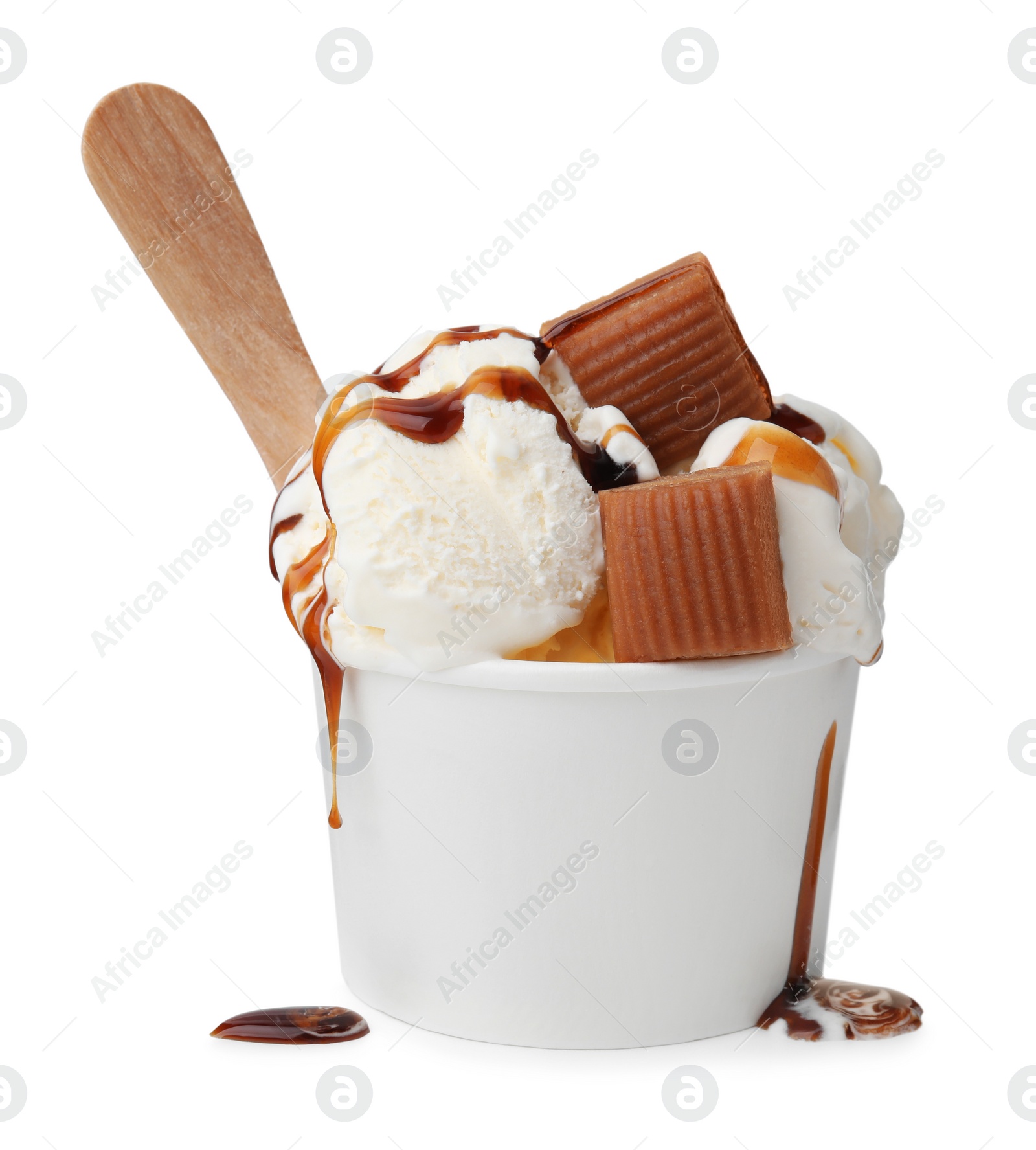 Photo of Scoops of delicious ice cream with caramel sauce and candies in paper cup isolated on white