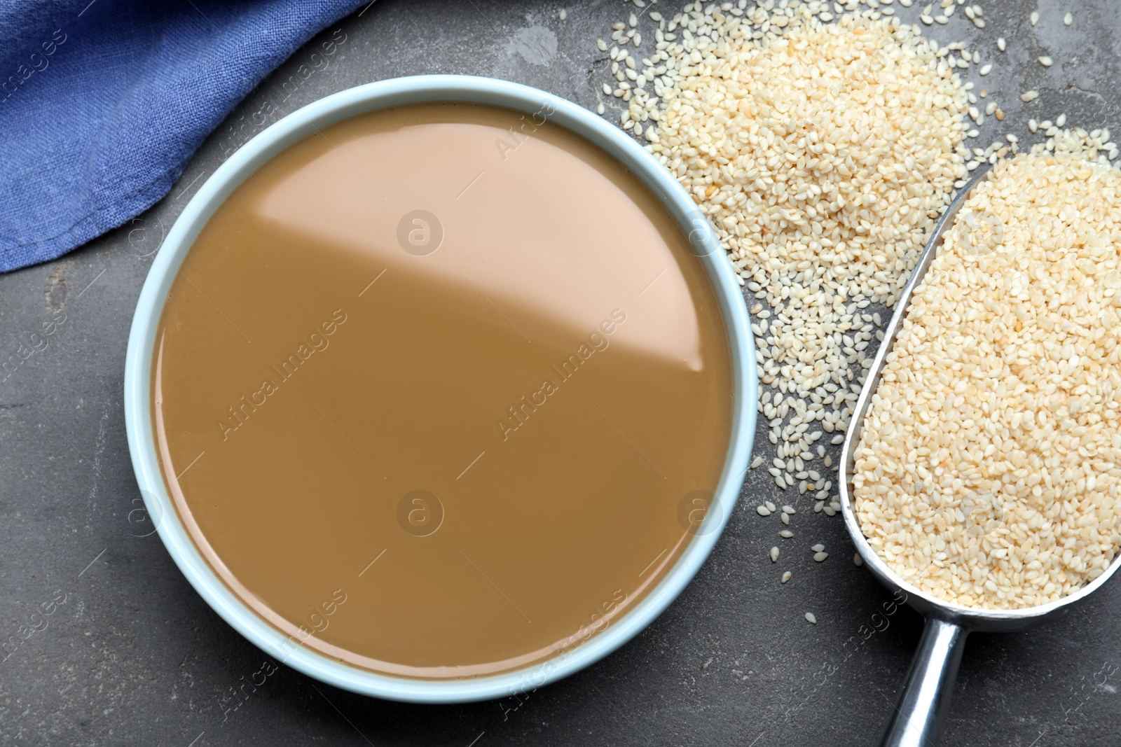 Photo of Tasty sesame paste, scoop and seeds on grey table, flat lay