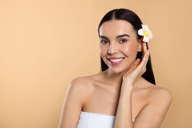 Photo of Young woman with plumeria flower in hair on beige background, space for text. Spa treatment