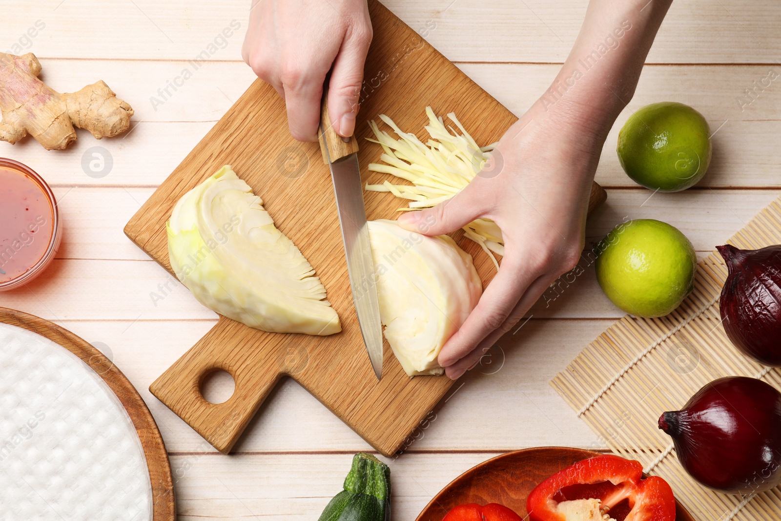 Photo of Making delicious spring rolls. Woman cutting cabbage at wooden table, top view