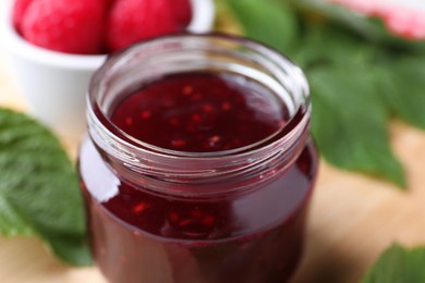 Glass jar of delicious raspberry jam on table, closeup