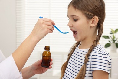 Photo of Doctor giving cough syrup to girl in clinic