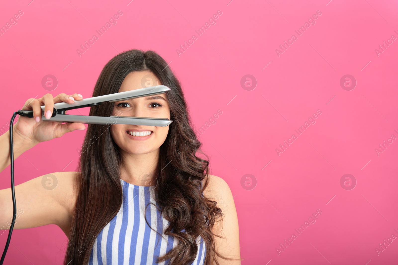 Photo of Young woman with modern hair iron on pink background, space for text