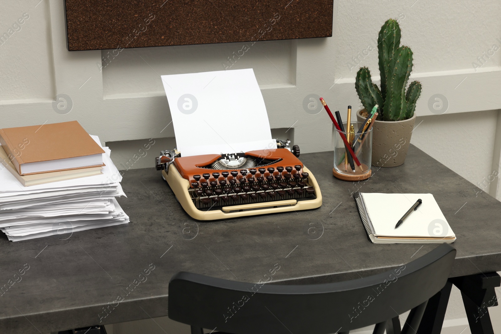 Photo of Typewriter and stack of papers on dark table in room. Writer's workplace