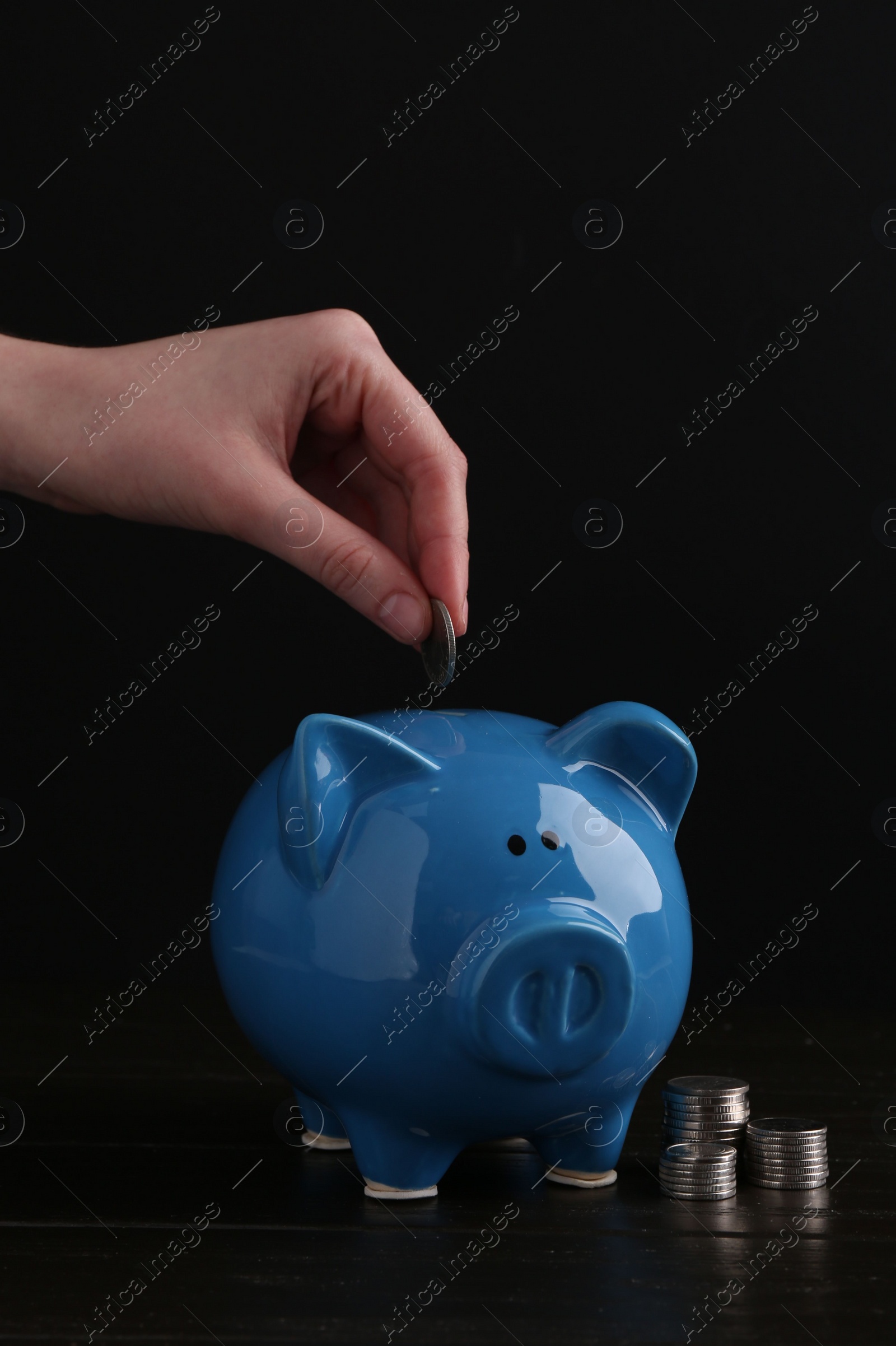 Photo of Financial savings. Woman putting coin into piggy bank at wooden table, closeup