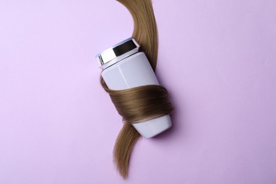Photo of Bottle wrapped in lock of hair on violet background, top view. Natural cosmetic product