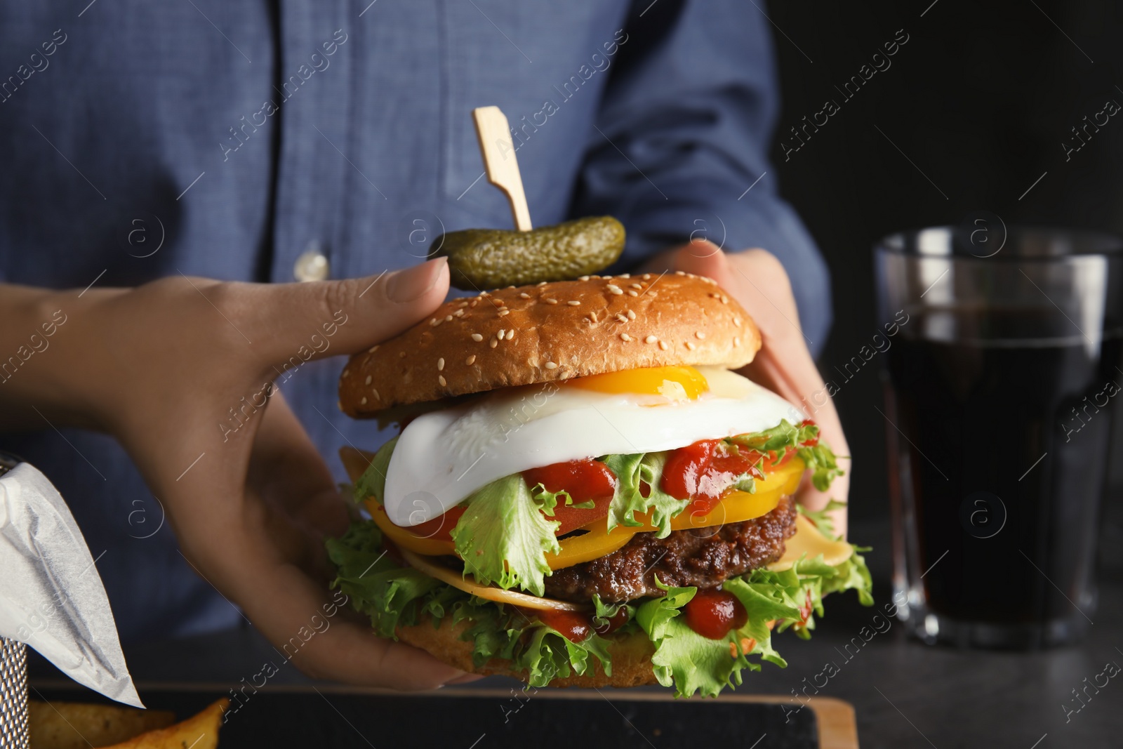 Photo of Woman holding tasty burger with fried egg over table, closeup