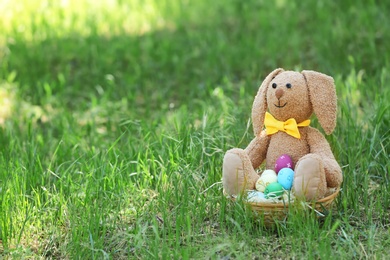 Photo of Toy bunny and basket with Easter eggs on grass