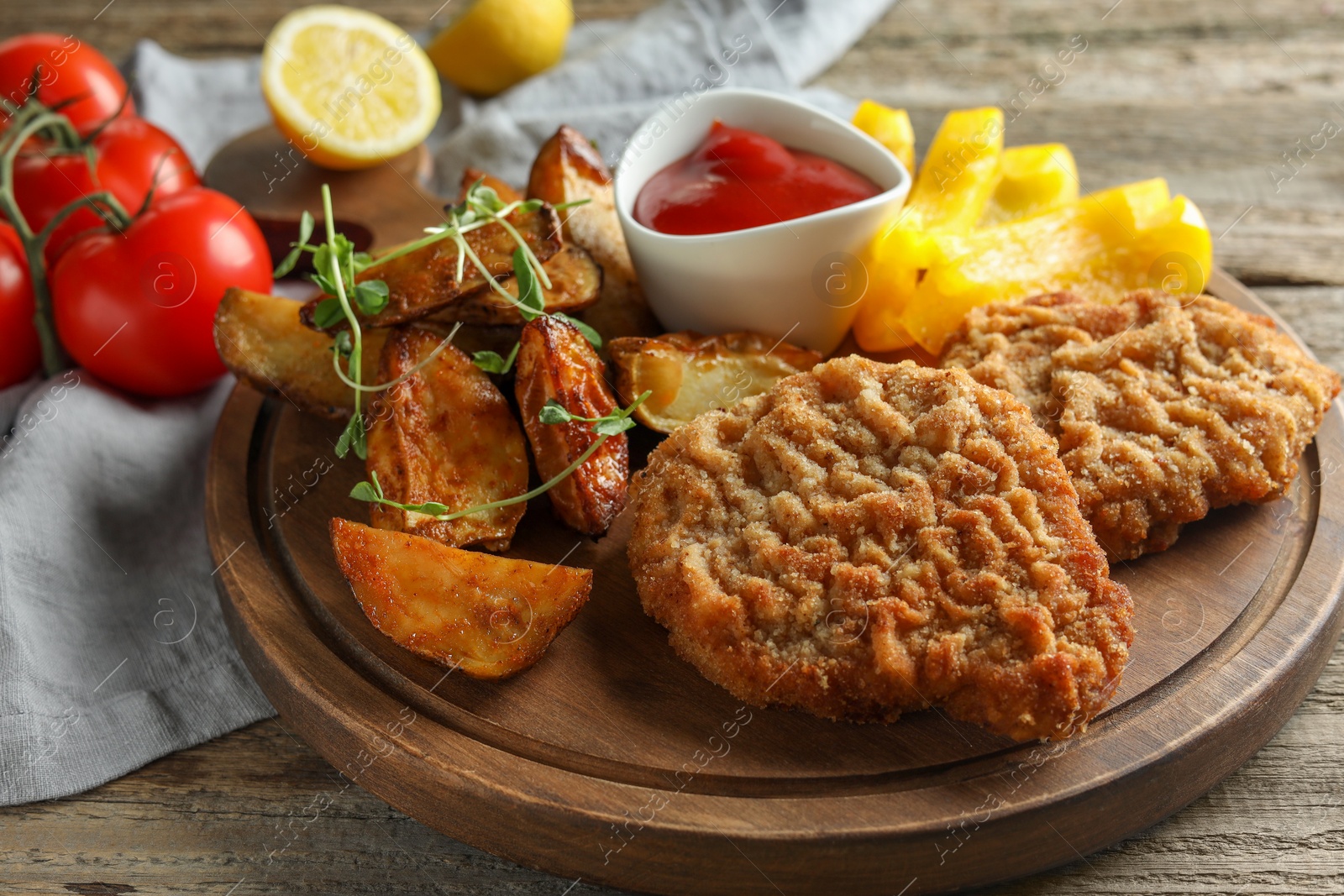 Photo of Tasty schnitzels served with potatoes, ketchup and vegetables on wooden table, closeup