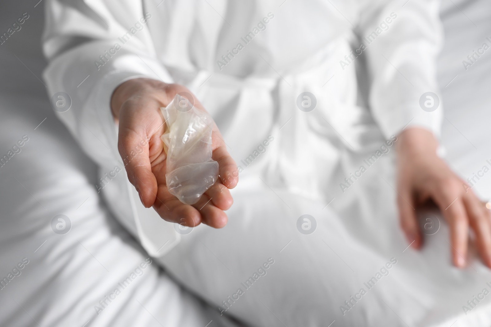 Photo of Woman holding unrolled condom on bed, closeup. Safe sex