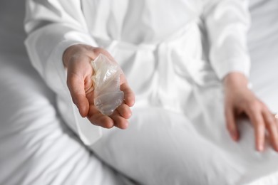Photo of Woman holding unrolled condom on bed, closeup. Safe sex