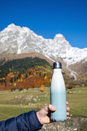 Photo of Boy holding thermo bottle with drink in mountains on sunny day, closeup