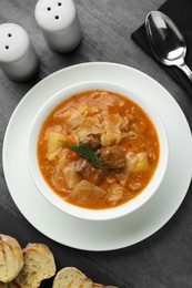 Photo of Tasty cabbage soup with meat, carrot and dill served on black table, flat lay
