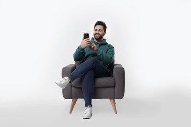 Photo of Happy young man using smartphone in armchair on white background
